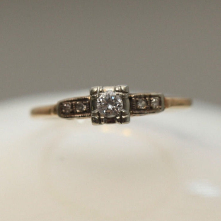 Straight-on view of 1940s vintage 14K two-tone diamond engagement ring with illusion head and stepped shoulders, displayed on marble background.