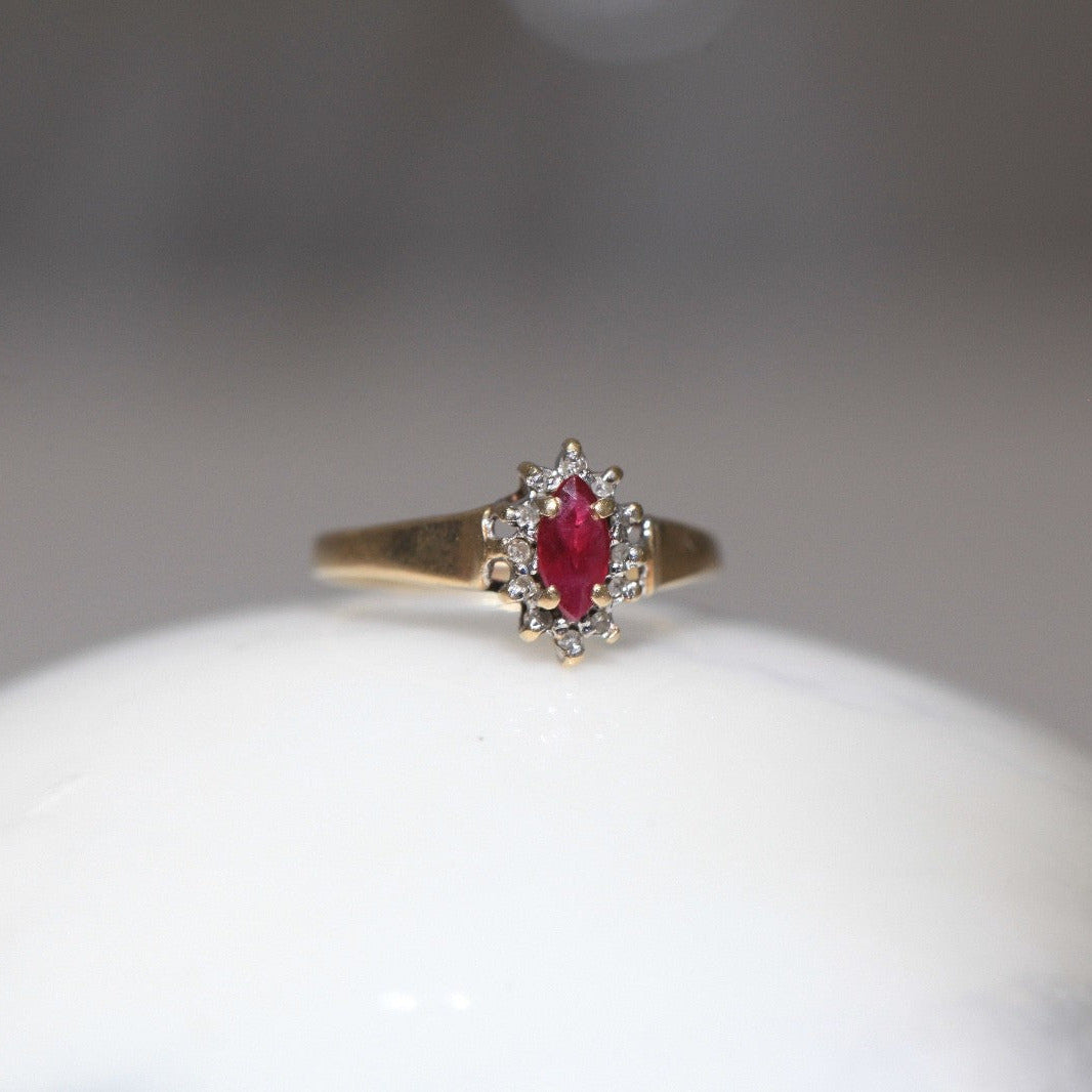 1970s vintage 10K gold ruby and diamond halo ring, marquise cut ruby with diamond cluster, photographed on marble surface