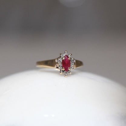 1970s vintage 10K gold ruby and diamond halo ring, marquise cut ruby with diamond cluster, photographed on marble surface