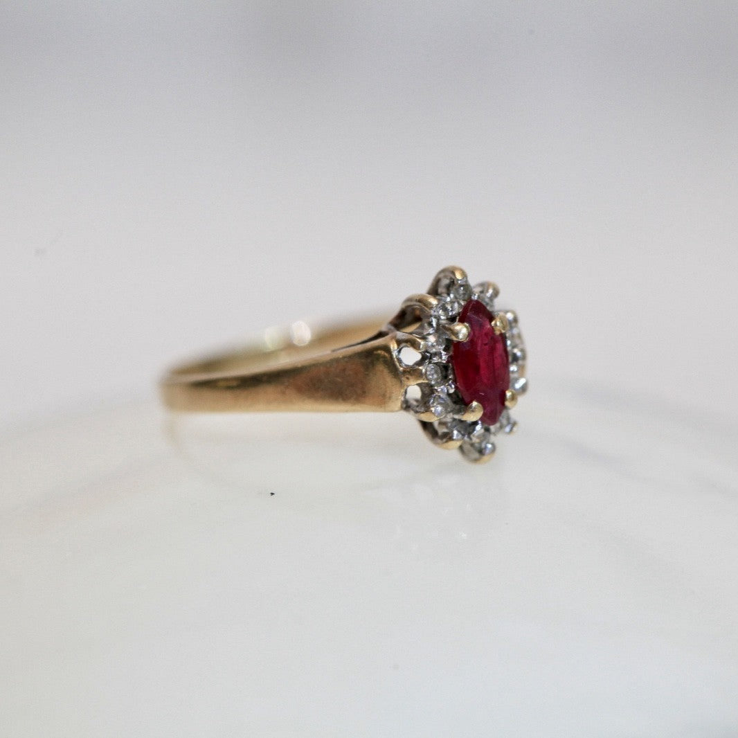 Angled view of 1970s vintage 10K gold ruby and diamond halo ring, marquise cut ruby with diamond cluster, photographed on white background