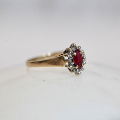 Angled view of 1970s vintage 10K gold ruby and diamond halo ring, marquise cut ruby with diamond cluster, photographed on white background