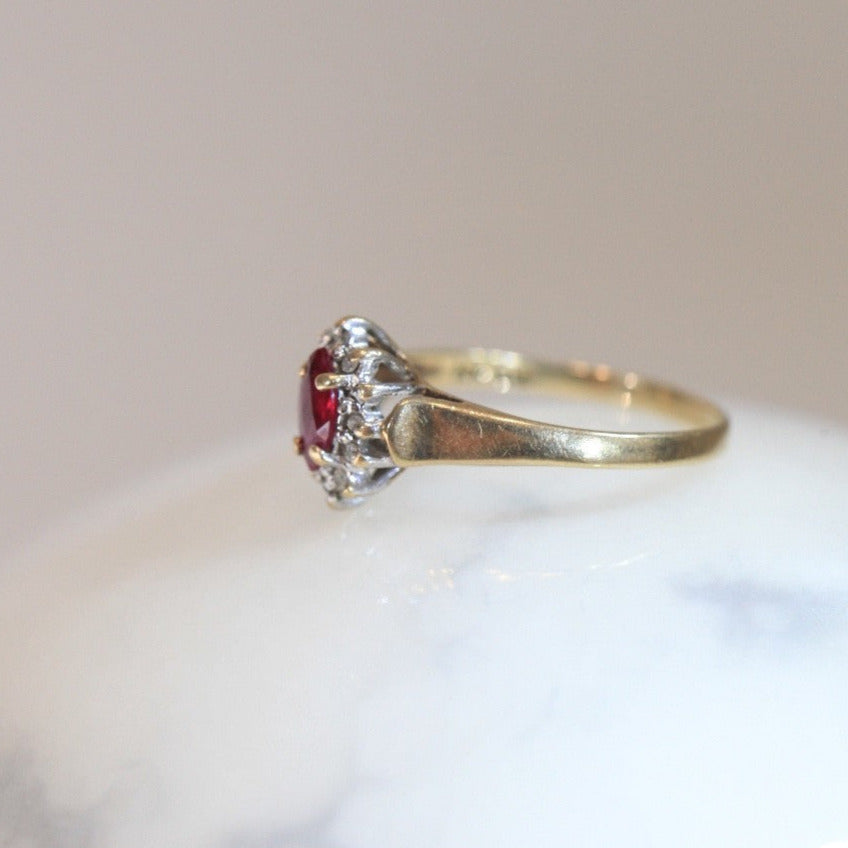 Profile view of 1970s vintage 10K gold ruby and diamond halo ring, marquise cut ruby with diamond cluster, photographed on white marble surface