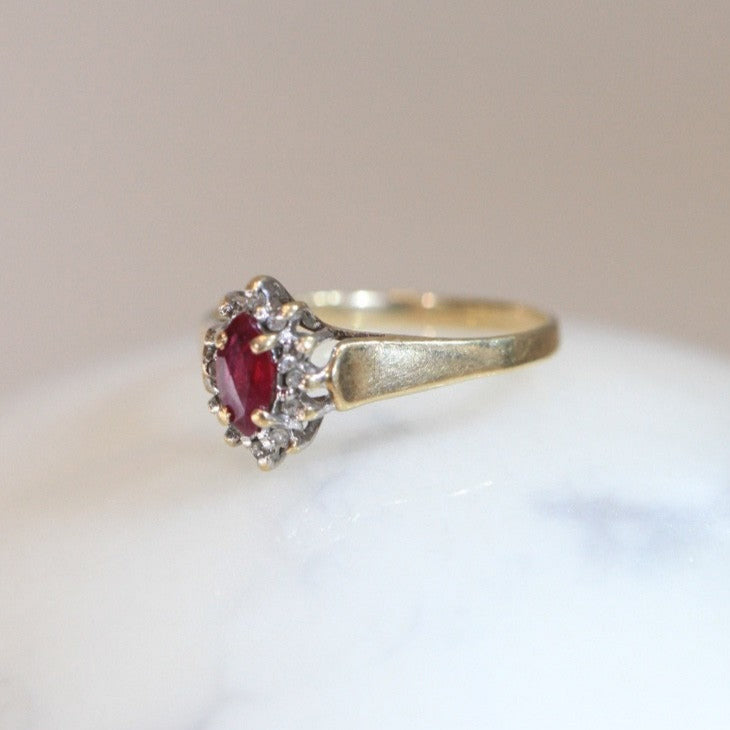 Side view of 1970s vintage 10K gold ruby and diamond halo ring, marquise cut ruby with diamond cluster, photographed on white marble surface
