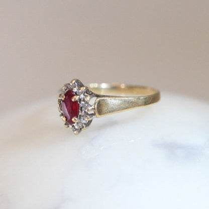 Side view of 1970s vintage 10K gold ruby and diamond halo ring, marquise cut ruby with diamond cluster, photographed on white marble surface