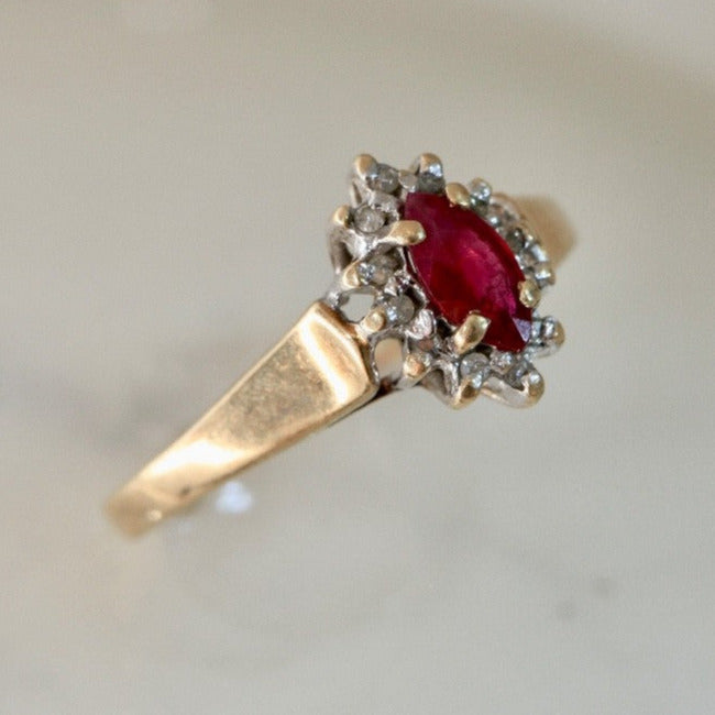 Close-up of 1970s vintage 10K gold ruby and diamond halo ring, marquise cut ruby with diamond cluster, photographed on white marble surface