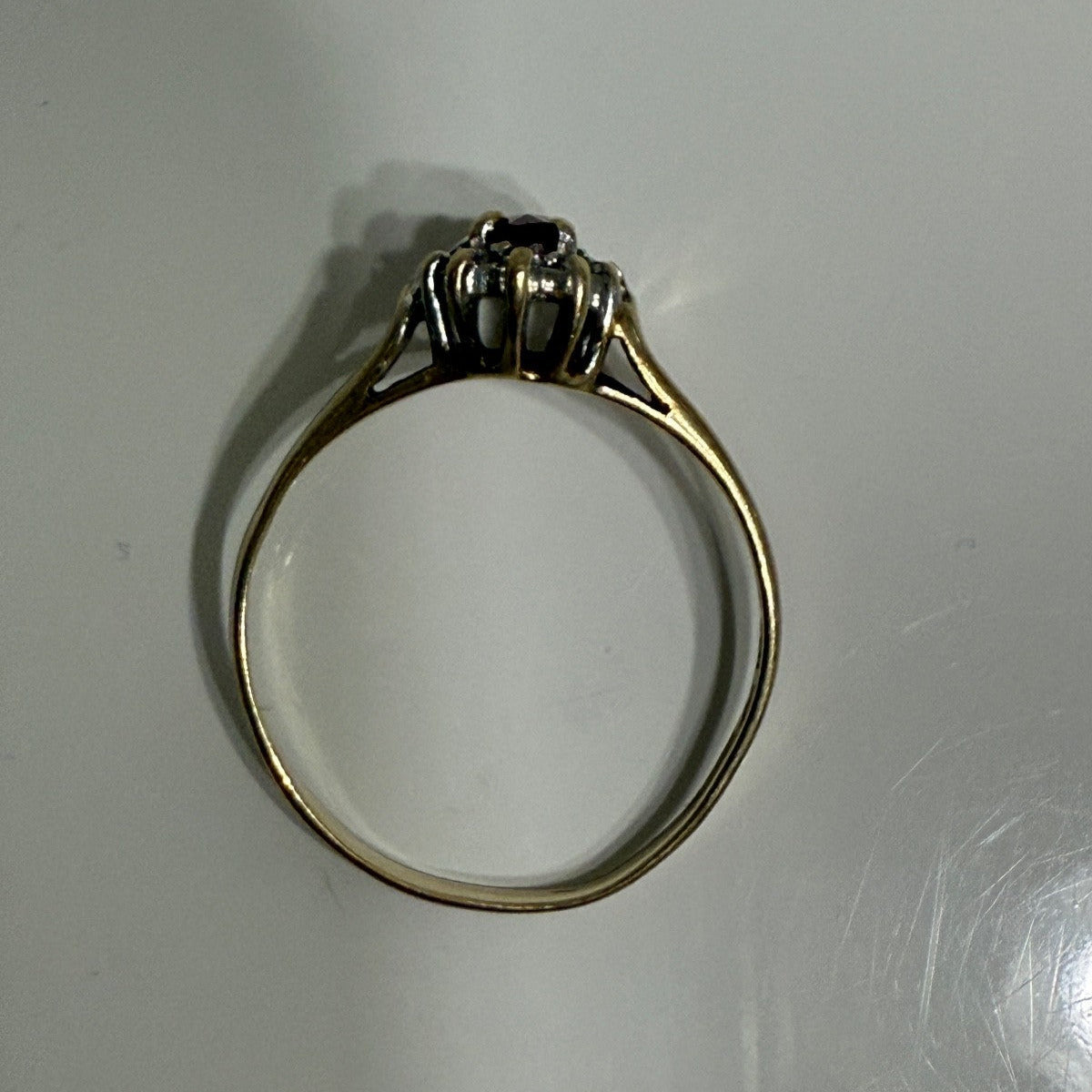 Side profile of 1970s vintage 10K gold ruby and diamond halo ring, marquise cut with raised gallery setting, photographed on gray surface