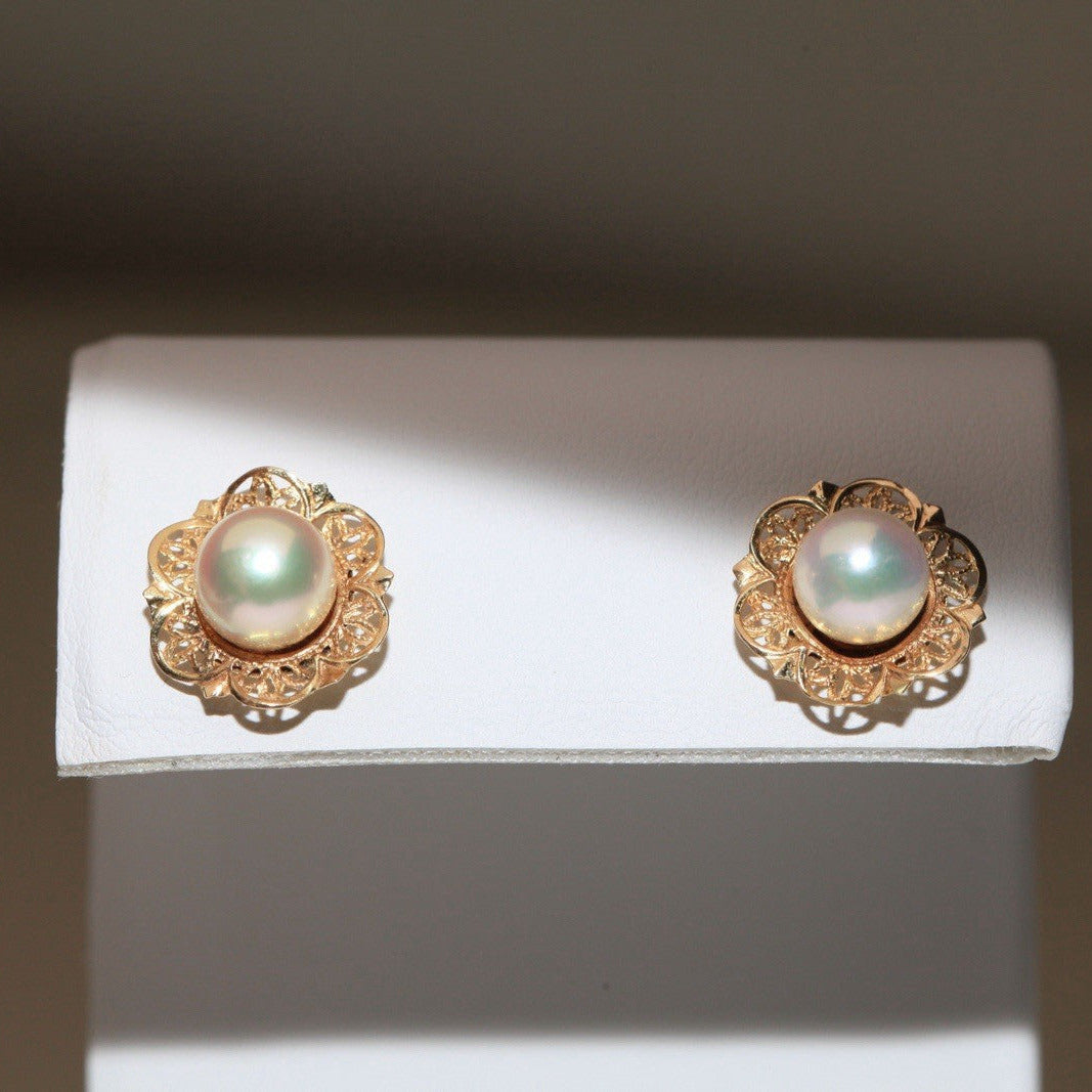 1960s vintage 14K yellow gold filigree flower stud earrings with cultured pearls displayed on a white card against a dark background