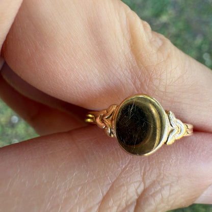Front view of antique Edwardian 14K gold oval signet ring on a finger, showing polished signet face