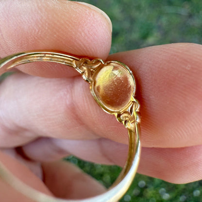 Close-up of antique Edwardian 14K gold oval signet ring held between fingers, showing smooth unengraved face