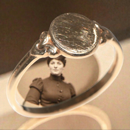 Antique Edwardian 14K gold oval signet ring with engraved wear marks, styled over vintage portrait background