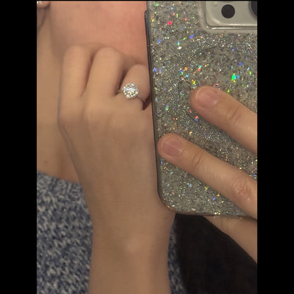 Hand wearing an 18K white gold diamond halo ring, photographed in a mirror reflection
