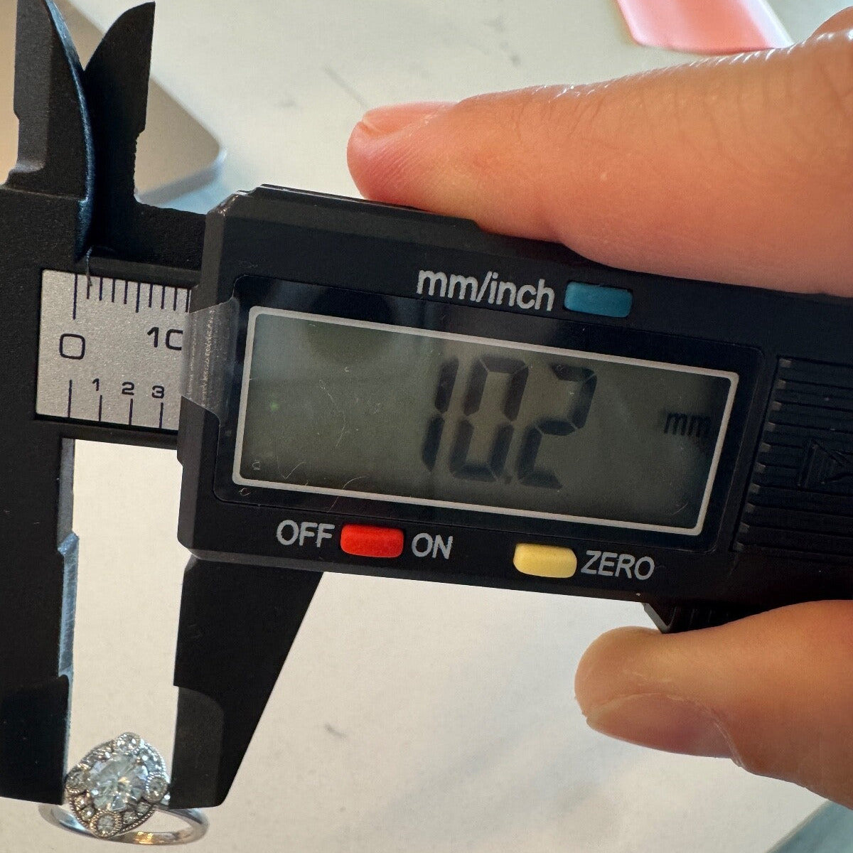 Digital caliper measuring the face of an 18K white gold diamond halo ring at 10.2 mm