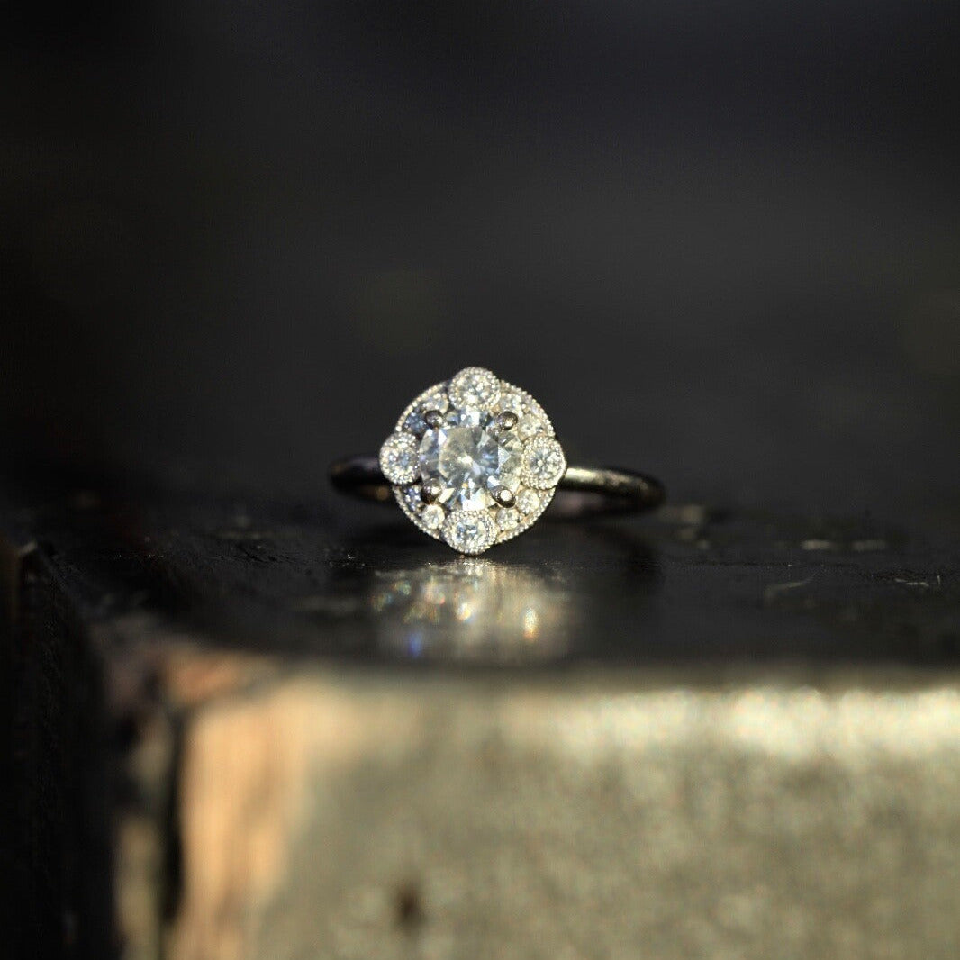 Laurence Bruyninckx 18K white gold diamond halo ring photographed on a dark surface with soft-focus background
